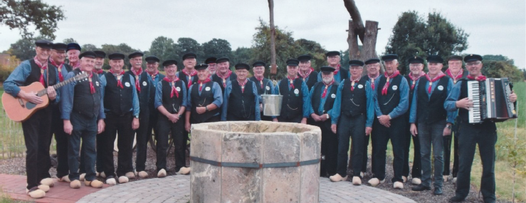 Das Foto (©Heimatverein Hoogstede-Arkel e.V. – zur Veröffentlichung freigegeben) zeigt die Heimatsänger vor dem Brunnen im Familiengoarn in Hoogstede