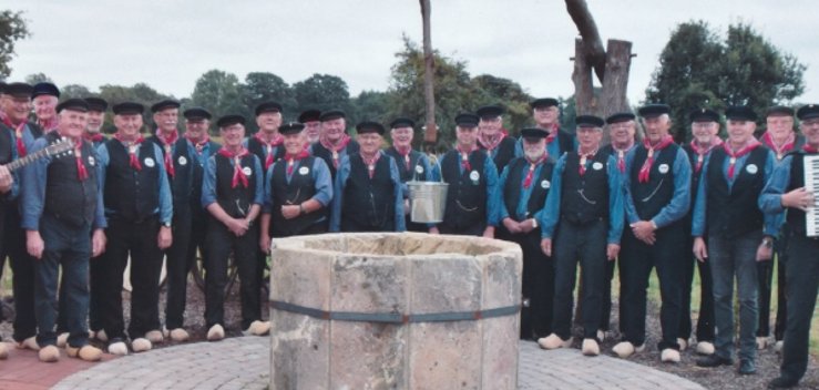Das Foto (©Heimatverein Hoogstede-Arkel e.V. – zur Veröffentlichung freigegeben) zeigt die Heimatsänger vor dem Brunnen im Familiengoarn in Hoogstede